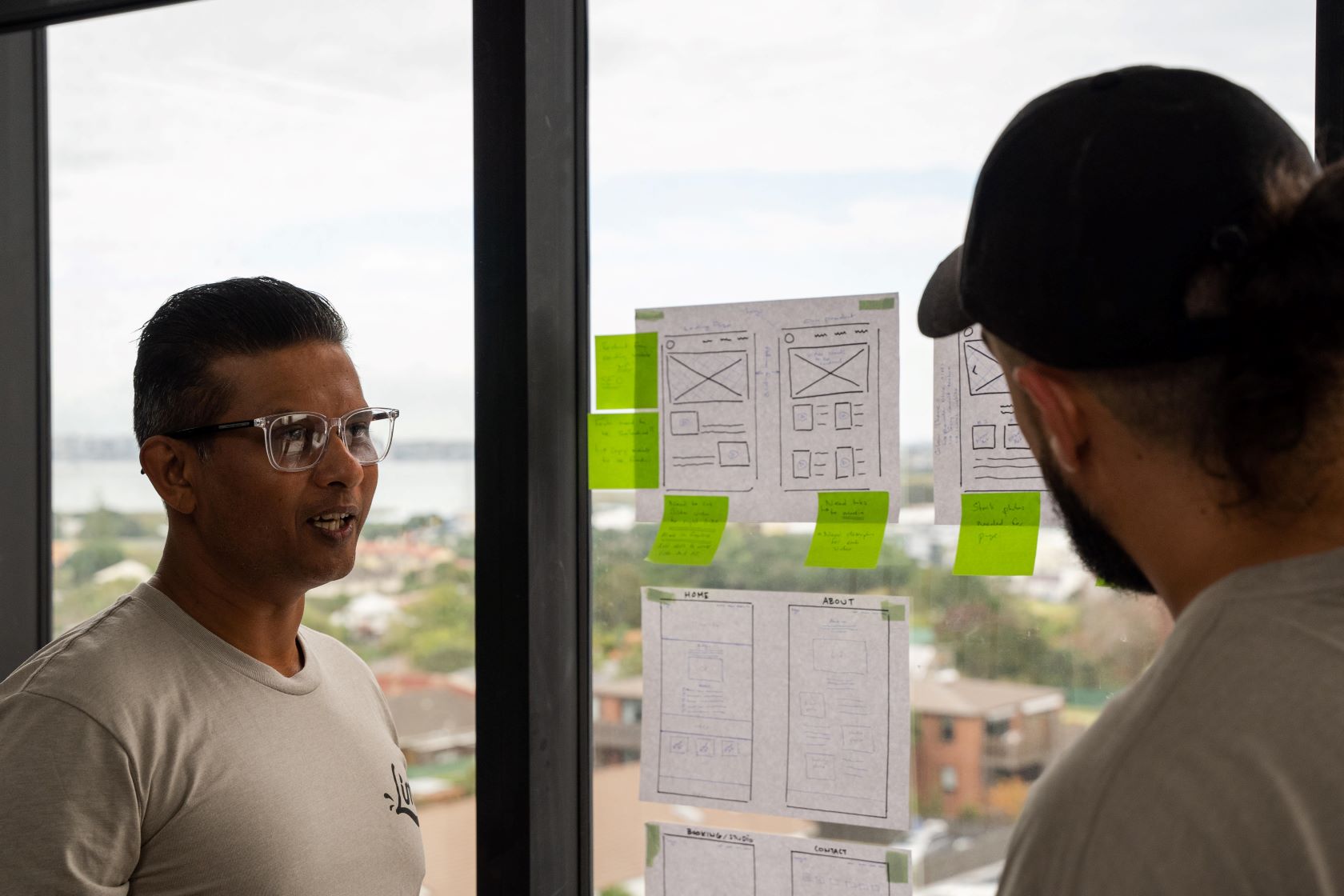 Two men talk about a document of website layout on a wall